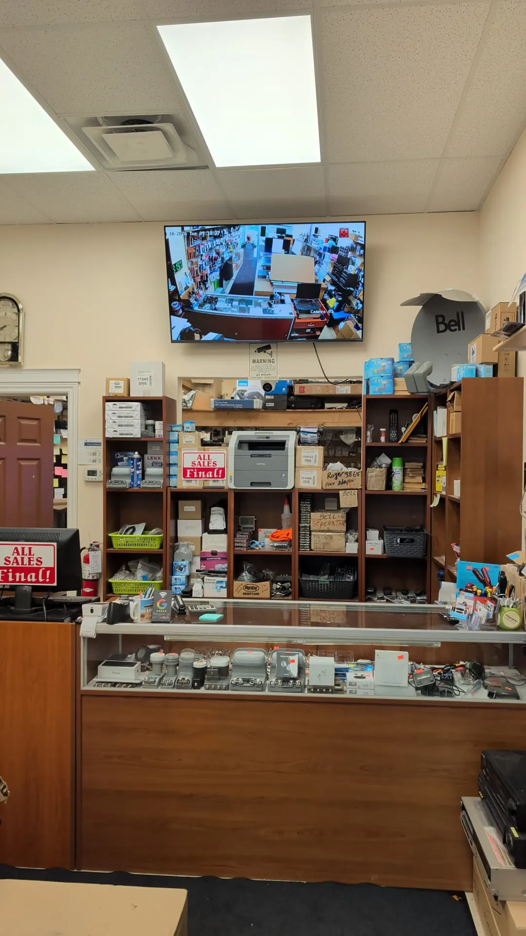 Inside the shop: the front counter and glass display case, shelves of stock and a Bell satellite dish on the top shelf